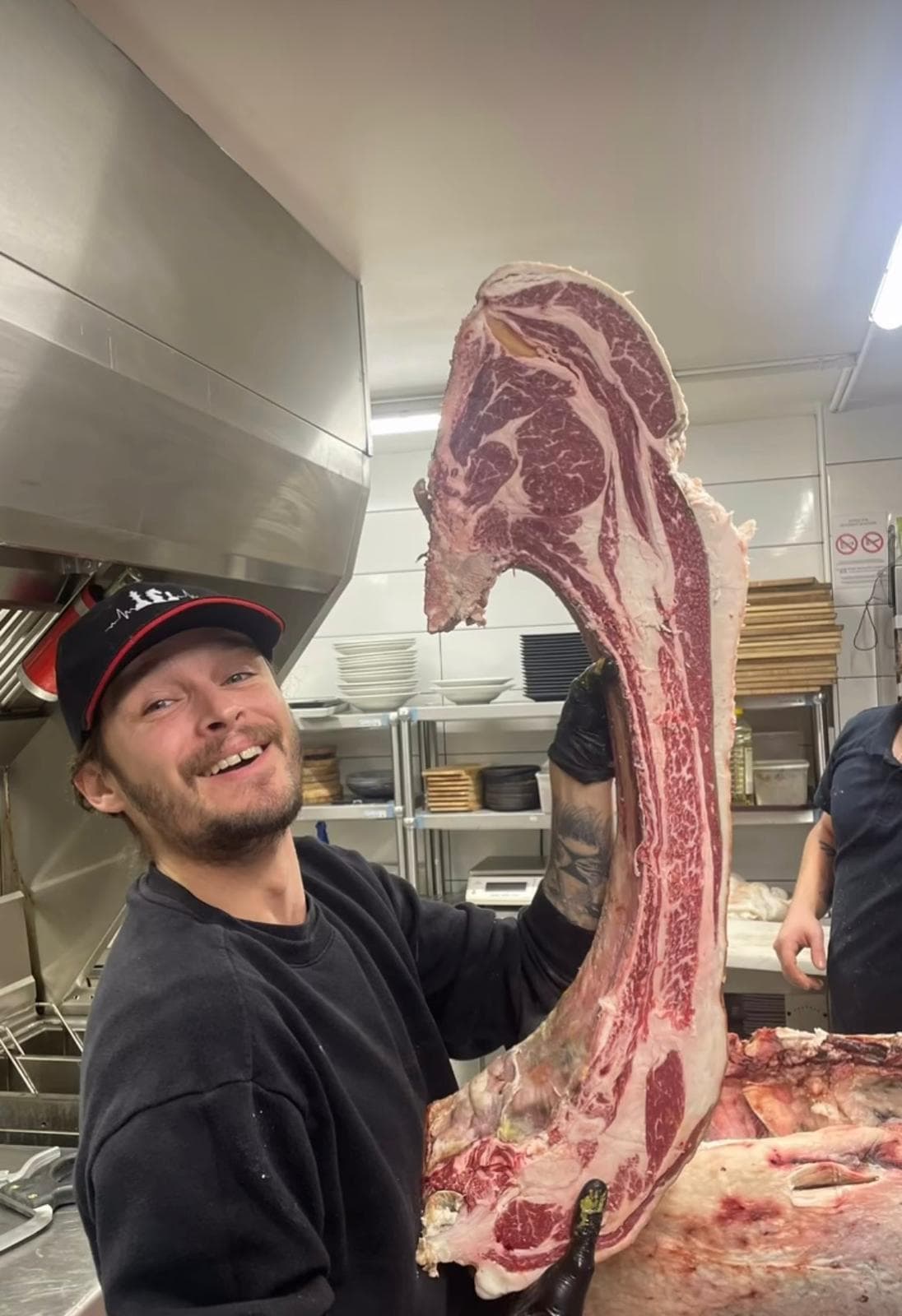Jeune cuisinier de l'équipe avec casquette ASBH présentant une côte de bœuf